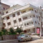 A white, four storey building in Izmit, Turkey, leans at a dangerous angle due to an earthquake. There is a road next to it with other buildings that are not affected.