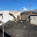 A white house and an outbuilding with piles of dark grey tephra around them