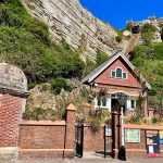 A steep furnicular railway track rises up some cliffs behind some red brick buildings