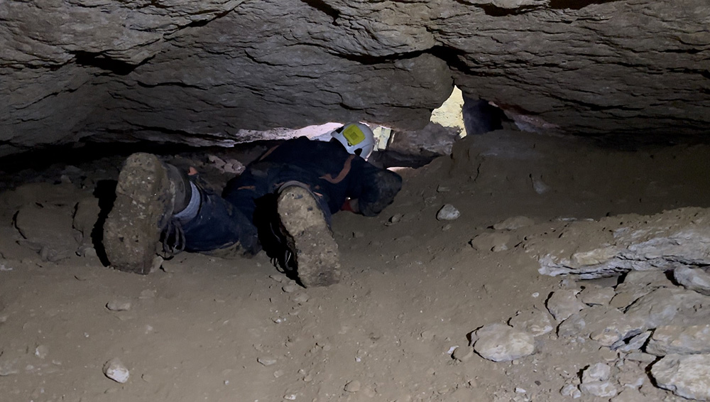 a man is crawling on his front through a very low cave