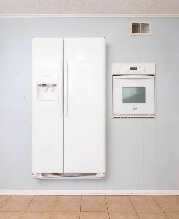 A fridge and wall oven installed awkwardly in a poorly designed kitchen setting.