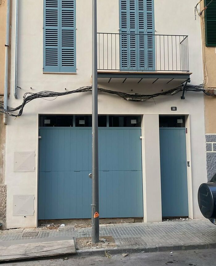 Design disaster featuring a mismatched balcony and doors with a utility pole obstructing garage access.