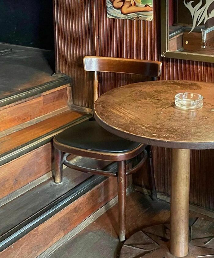 Design disaster: a table awkwardly blocking the path of stairs, with a mismatched chair and an ashtray on top.