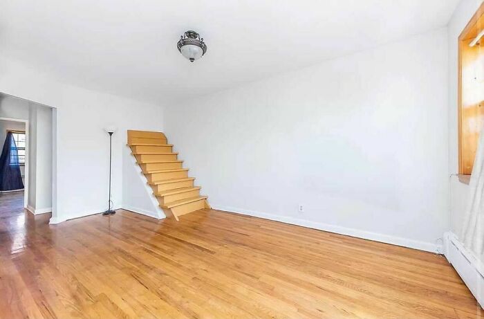 Room with a staircase leading to nowhere, showcasing a design disaster with wooden flooring and a single ceiling light.