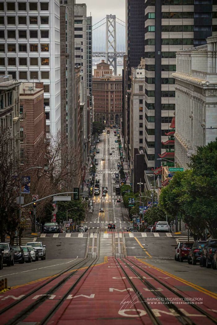 Street view towards gigantic Bay Bridge, surrounded by towering buildings, illustrating a massive urban landscape.