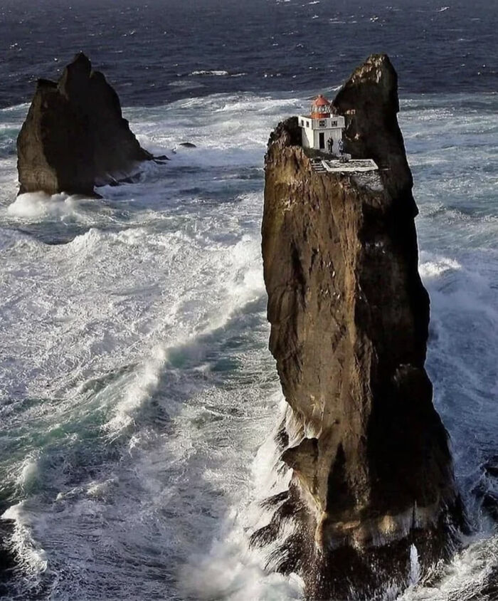 Lighthouse perched on towering sea stack surrounded by waves, a striking sight for anyone with megalophobia.