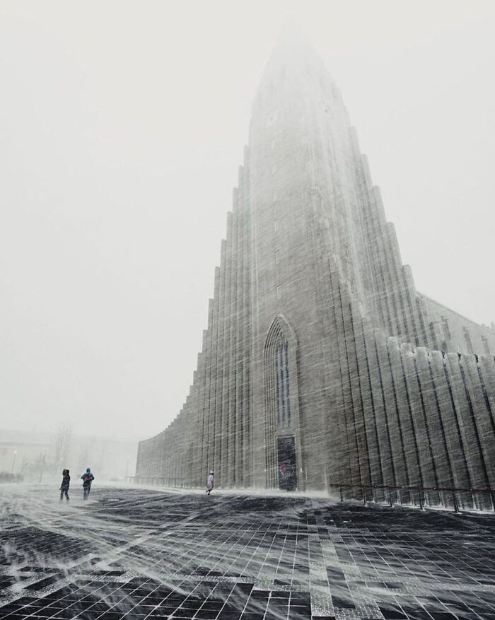 Gigantic cathedral in a snowstorm, towering over small figures below, illustrating megalophobia.