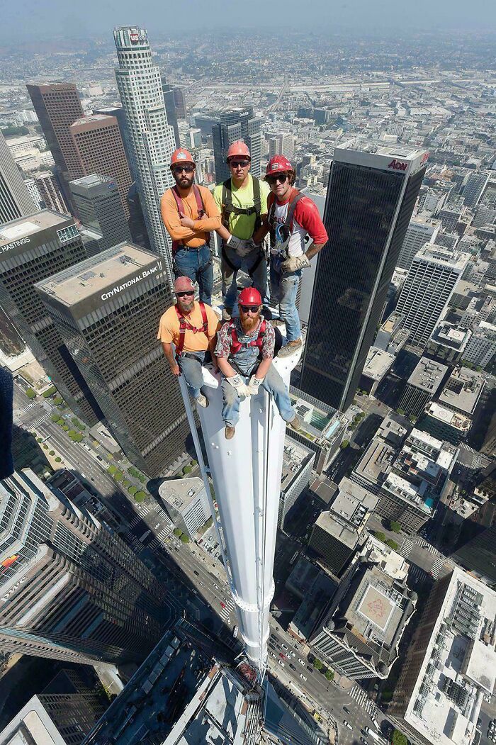 Workers perched atop a skyscraper spire, showcasing heights that trigger megalophobia against a vast cityscape.