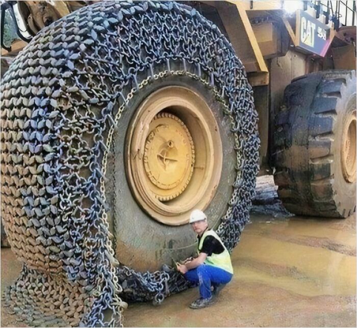 Gigantic tire with chains, worker kneels next to it. Perfect example for megalo­phobia enthusiasts.