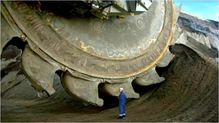 Person standing next to a massive industrial bucket wheel, highlighting a fear of gigantic things for those with megalophobia.