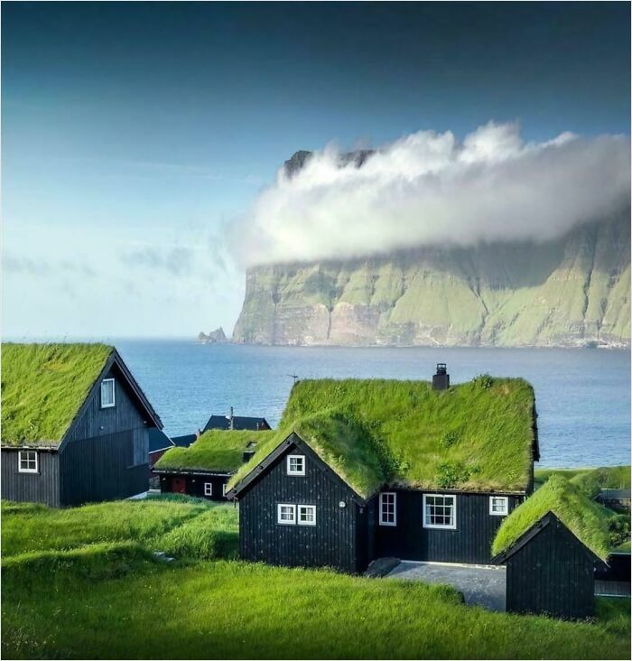 Grass-roofed houses with a gigantic backdrop of a towering cliff and ocean view, ideal for those without megalophobia.