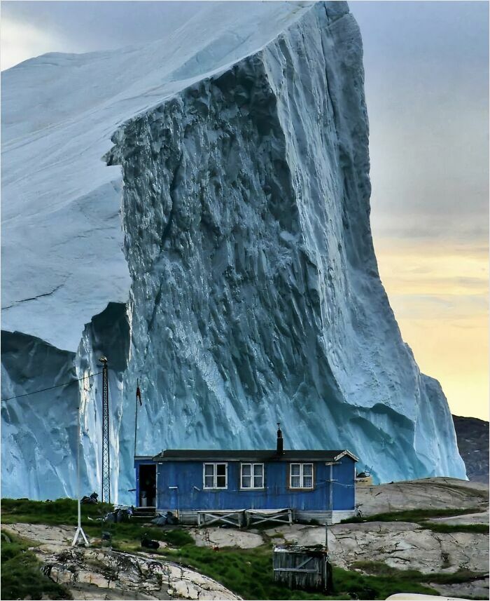 Small house dwarfed by a gigantic iceberg, highlighting megalophobia with intense scale contrast.