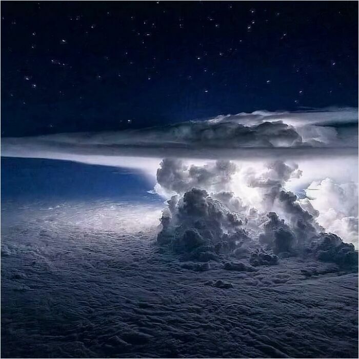 Massive storm cloud with bright lightning, viewed from above, evoking megalophobia against a starry night sky.