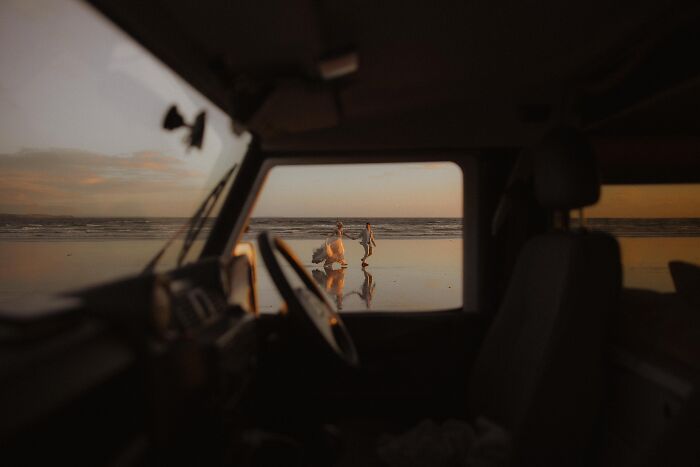 Couple walking on the beach at sunset, viewed from inside a vehicle, highlighting top wedding photos of 2024.