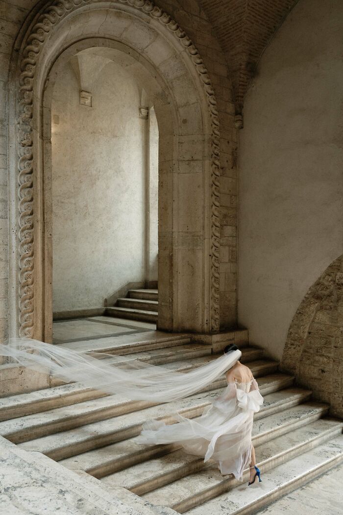 Bride in flowing gown and veil, ascending stone staircase, showcasing top wedding photos of 2024.