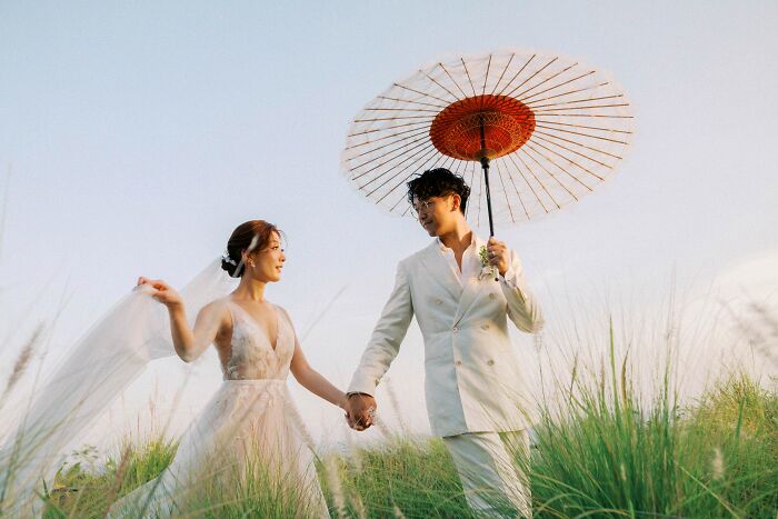 Bride and groom in a field, holding a parasol, showcasing top wedding photo of 2024.