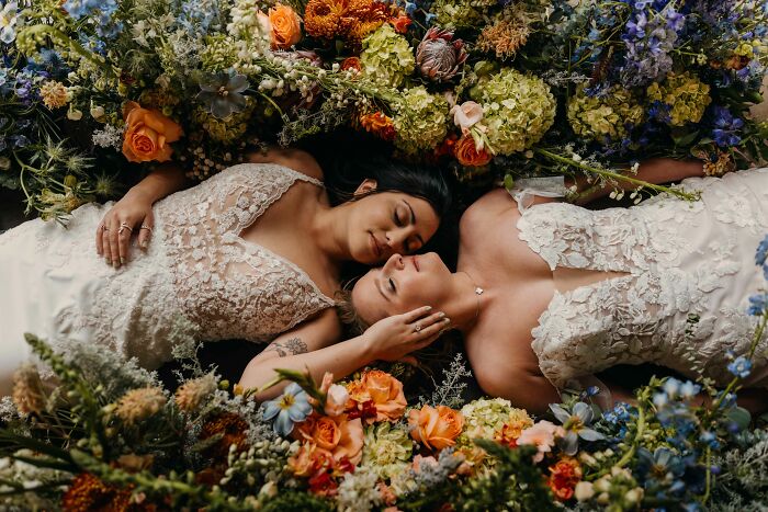 Brides in elegant gowns lie amid vibrant florals, exemplifying top wedding photography of 2024.