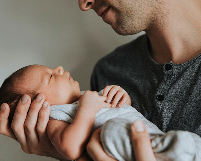 Father gently holding newborn baby, symbolizing breaking family tradition in naming practices.