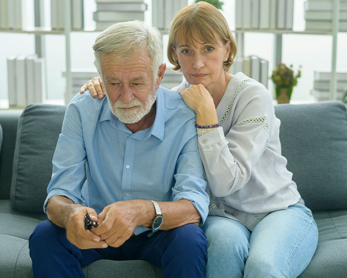 Older couple considering family tradition, looking contemplative on a couch.