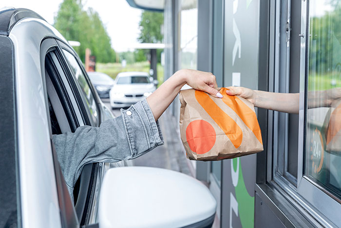 Drive-thru interaction with a customer receiving food in a brown paper bag from a window.