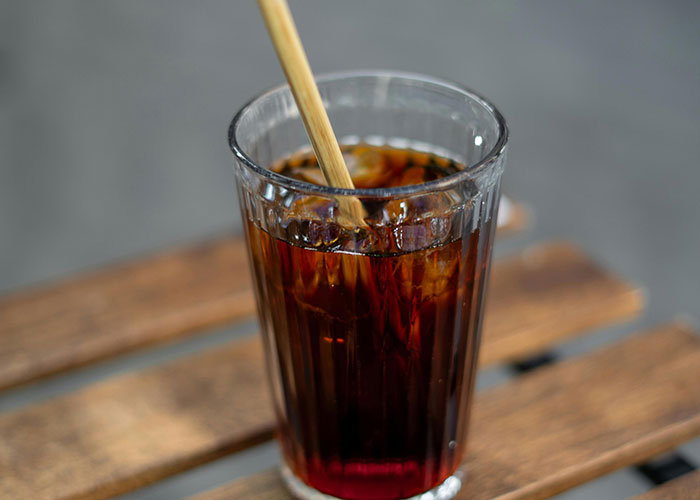 Glass of iced coffee with a bamboo straw on a wooden table, illustrating a creative frugal hack.