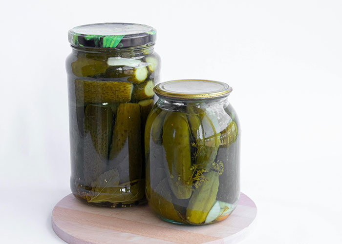 Jars of homemade pickles on a wooden stand; creative frugal hacks for saving cash.