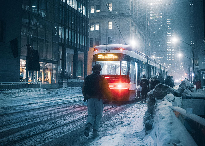 People walking through snowy city street at night, approaching a tram; an example of creative frugal transportation.