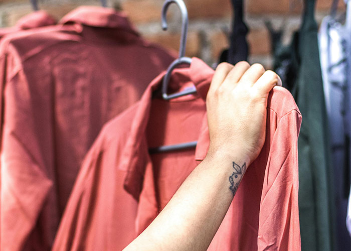 A person choosing a frugal clothing option, holding a pink shirt from a rack.