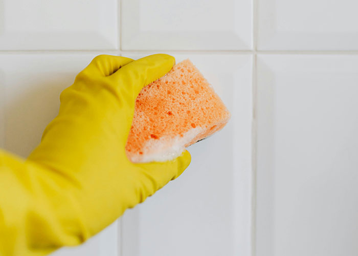 Gloved hand cleaning tiles with sponge, demonstrating a frugal hack.