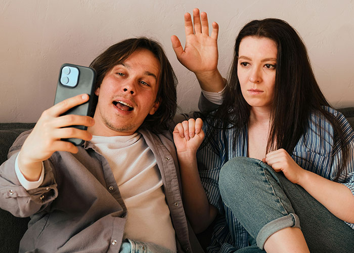 Young couple on a sofa, the man holding a phone, discussing Bahamas trip and family conflicts.