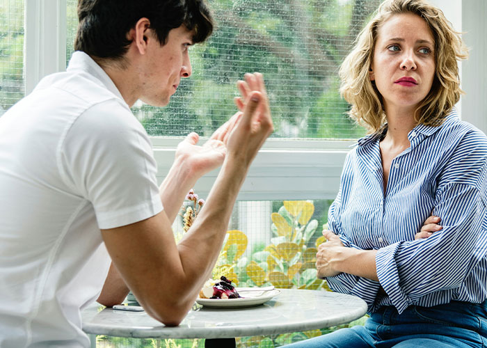 Couple having a tense discussion in a café, representing conflict over a Bahamas trip and Christmas plans.