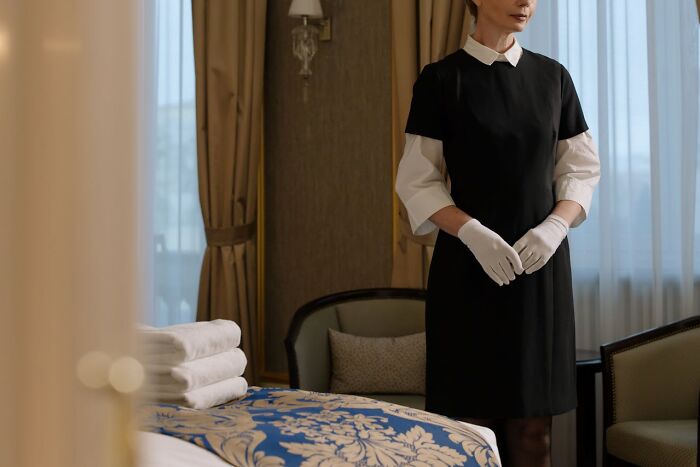 Casino employee in uniform, standing with folded hands in a hotel room, highlighting behind-the-scenes work.