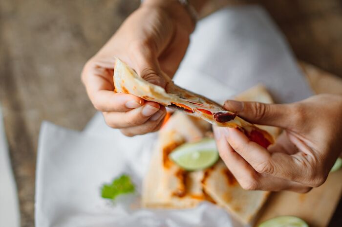 Hands holding a quesadilla with lime garnish, showing the detail behind casino dining experiences.