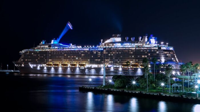 Cruise ship docked at night with bright lights, highlighting behind-the-scenes operations.