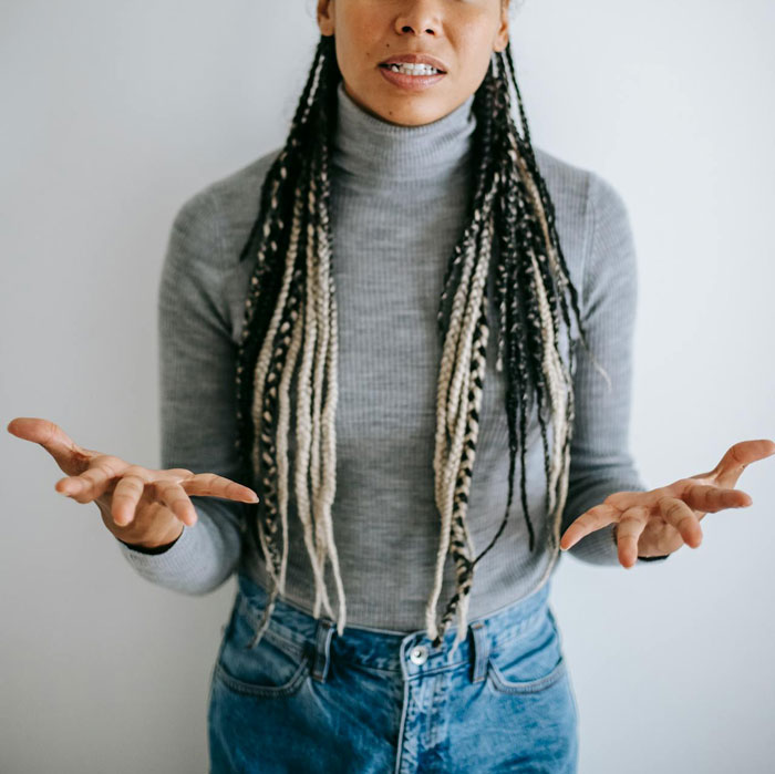 Woman gesturing emotionally in grey sweater and jeans, conveying tension.