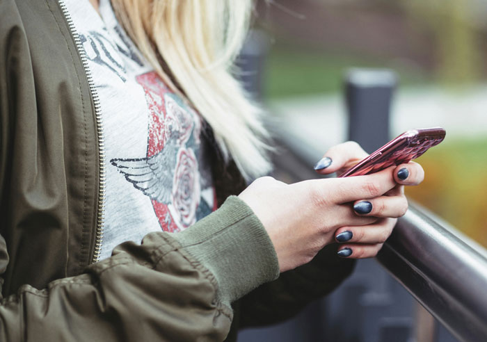 Woman using a smartphone outdoors, wearing a green jacket and graphic tee, prioritizing financial responsibility.