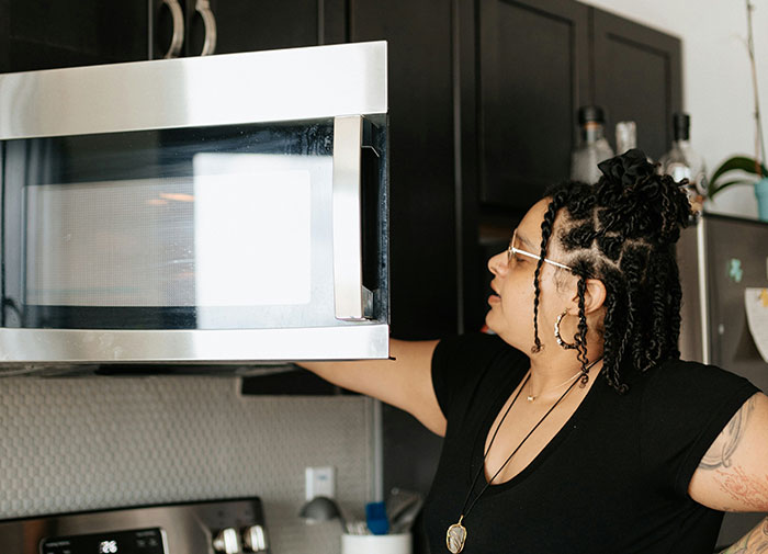 Person using microwave improperly, standing in kitchen.