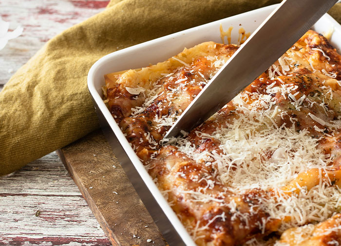 Using things wrong way: cutting lasagna with a large knife in a white baking dish.