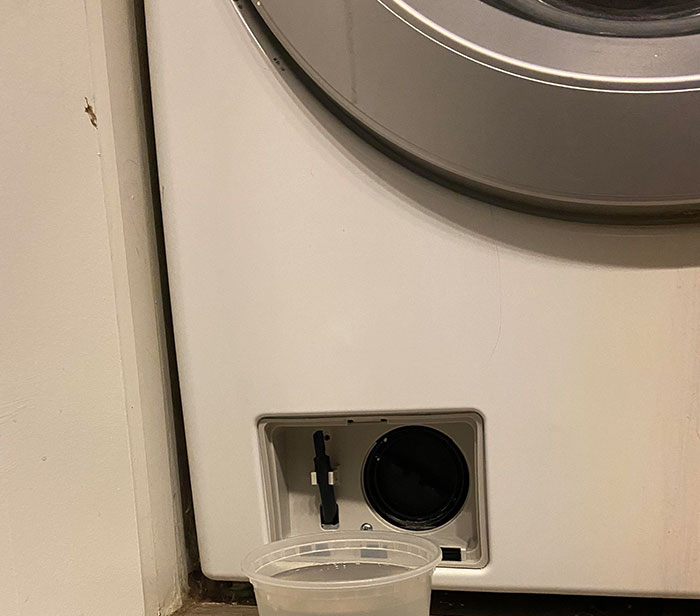 Plastic cup collecting leaking water from washing machine, illustrating using things the wrong way.