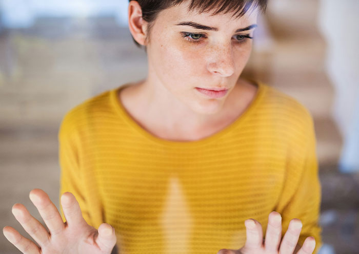 Person in a yellow sweater looking thoughtfully out a window, illustrating using-things-wrong-way theme.