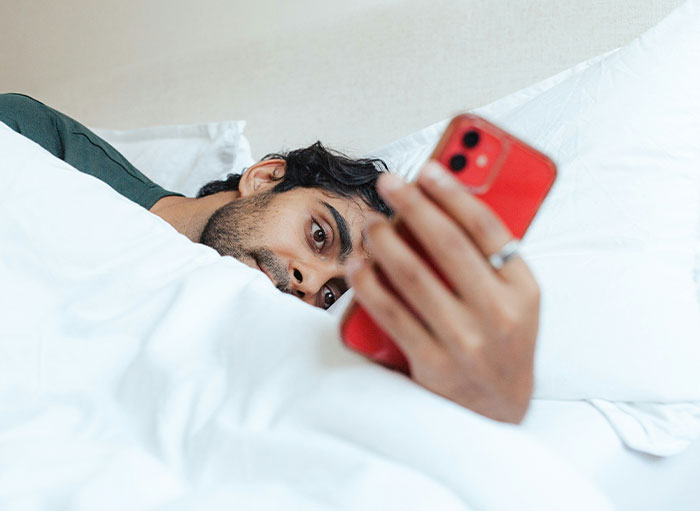 Person using a smartphone in bed in a unique way, focusing on screen.