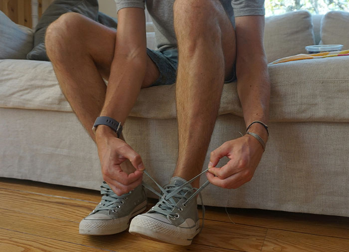 Man tying shoelaces on sneakers while seated, illustrating using things the wrong way.