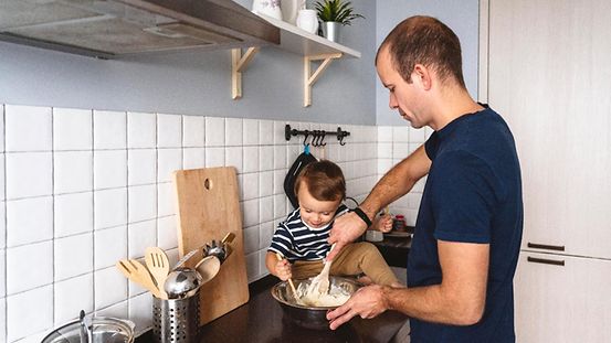 Vater mit Kind bereitet Essen in der Küche zu.