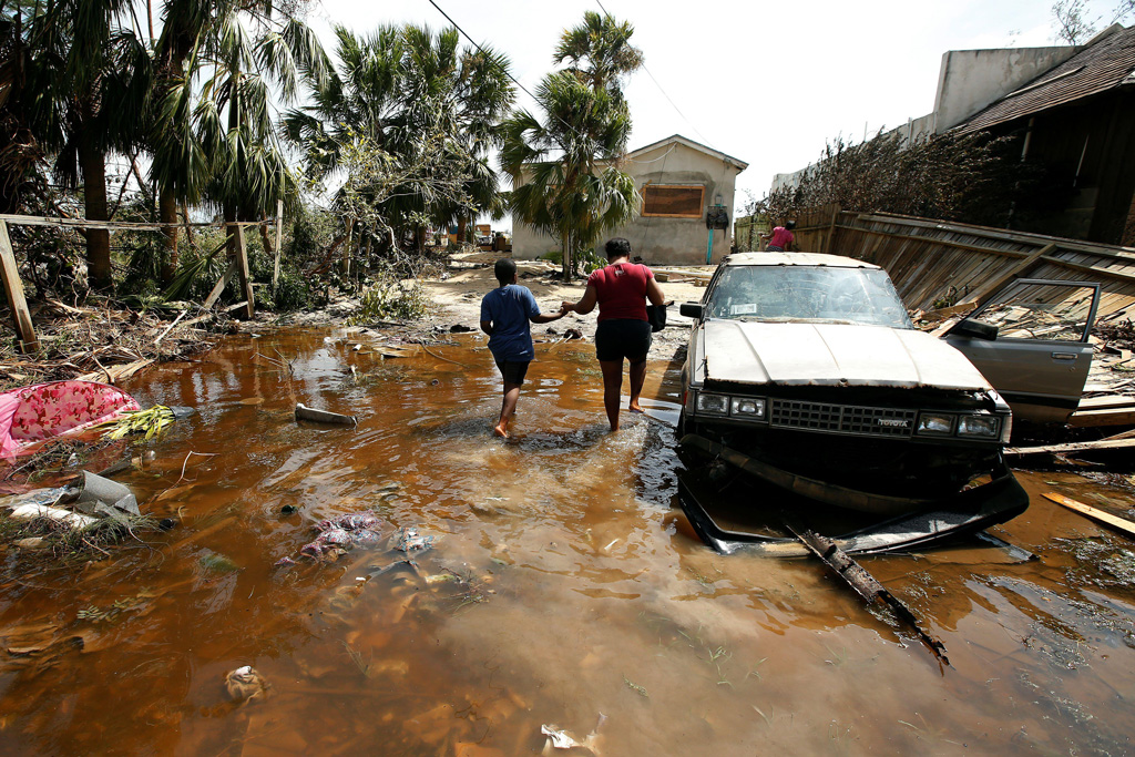 A woman and a child walk into their flooded house in the Bahamas after Hurricane Matthew