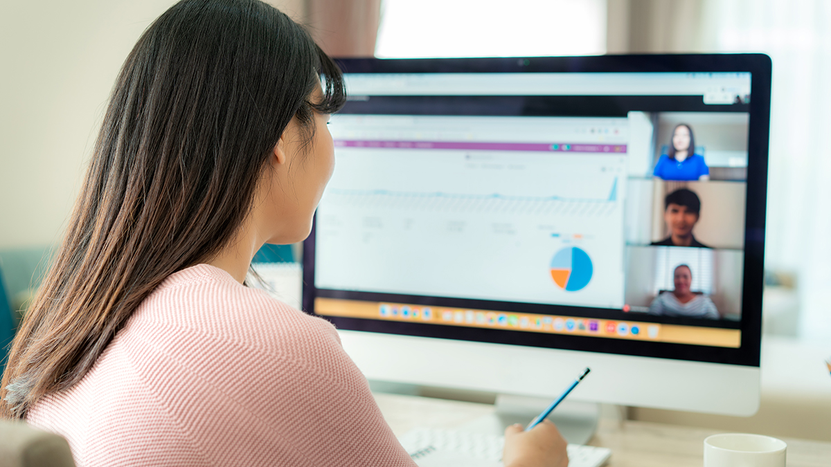 Back view of Asian business woman talking to her colleagues about plan in video conference. Multiethnic business team using computer for a online meeting in video call. Group of people smart working from home.