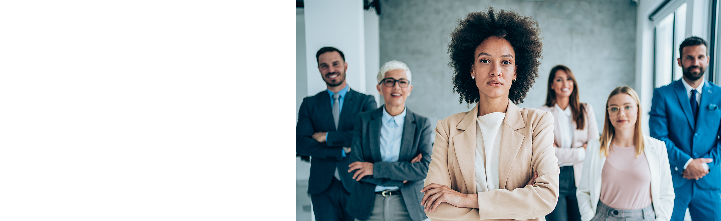 powerful Black woman in business attire standing with arms crossed in front of her diverse team of colleagues.