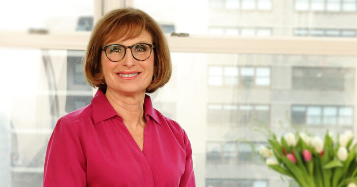 headshot of Lorraine Hariton, she is wearing a pink blouse and facing the viewer, smiling.