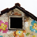 An old brick house with cross stitched flowers over it.