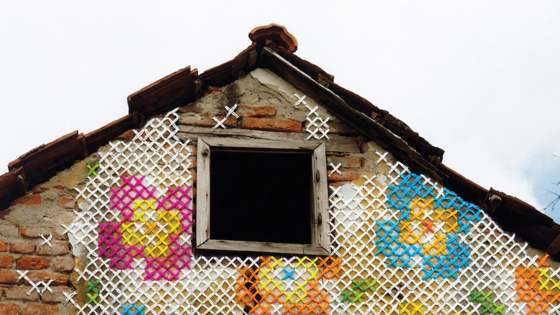 An old brick house with cross stitched flowers over it.