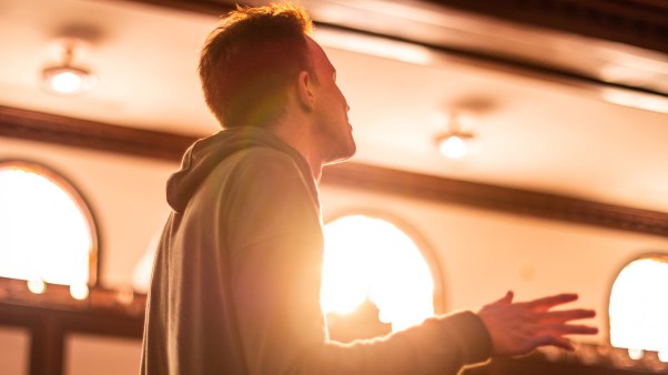 A student worshiping at the Asbury Revival with a bright light shining through a window near his heart.